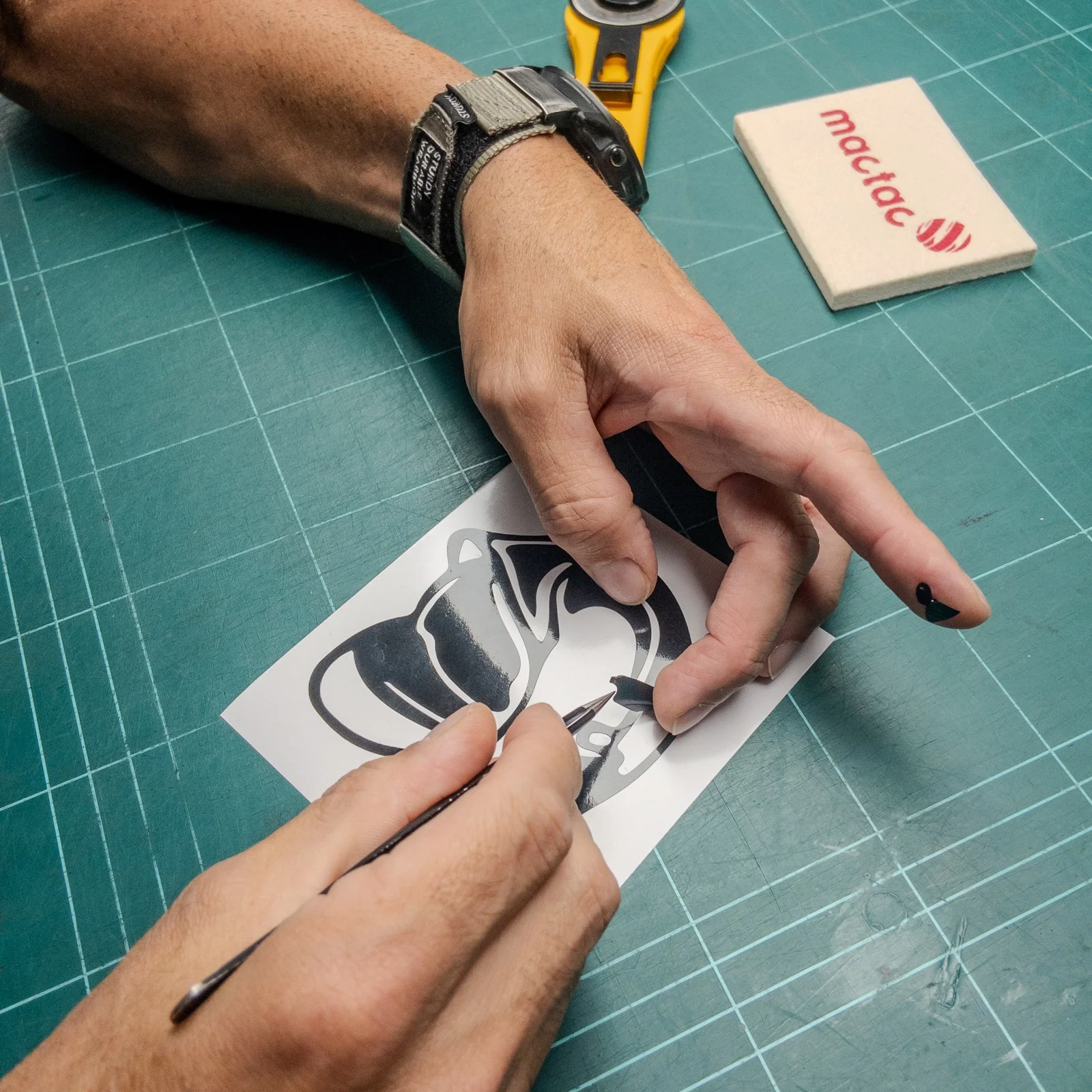 Manos pelando a mano con un punzón una pegatina de vinilo de corte negro sobre una alfombrilla de corte verde