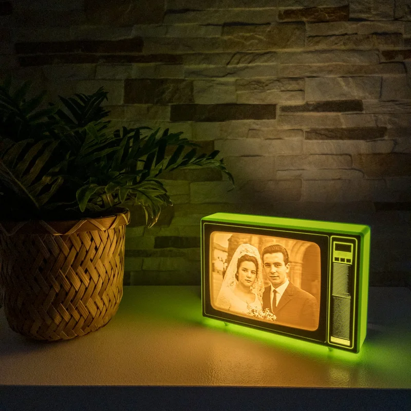 TV retro de Brilla verde encendida en una estantería junto a una planta, con una foto de boda antigua iluminada en luz cálida